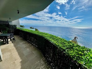 Une terrasse avec vue sur l’océan, une table avec des chaises et une haie.