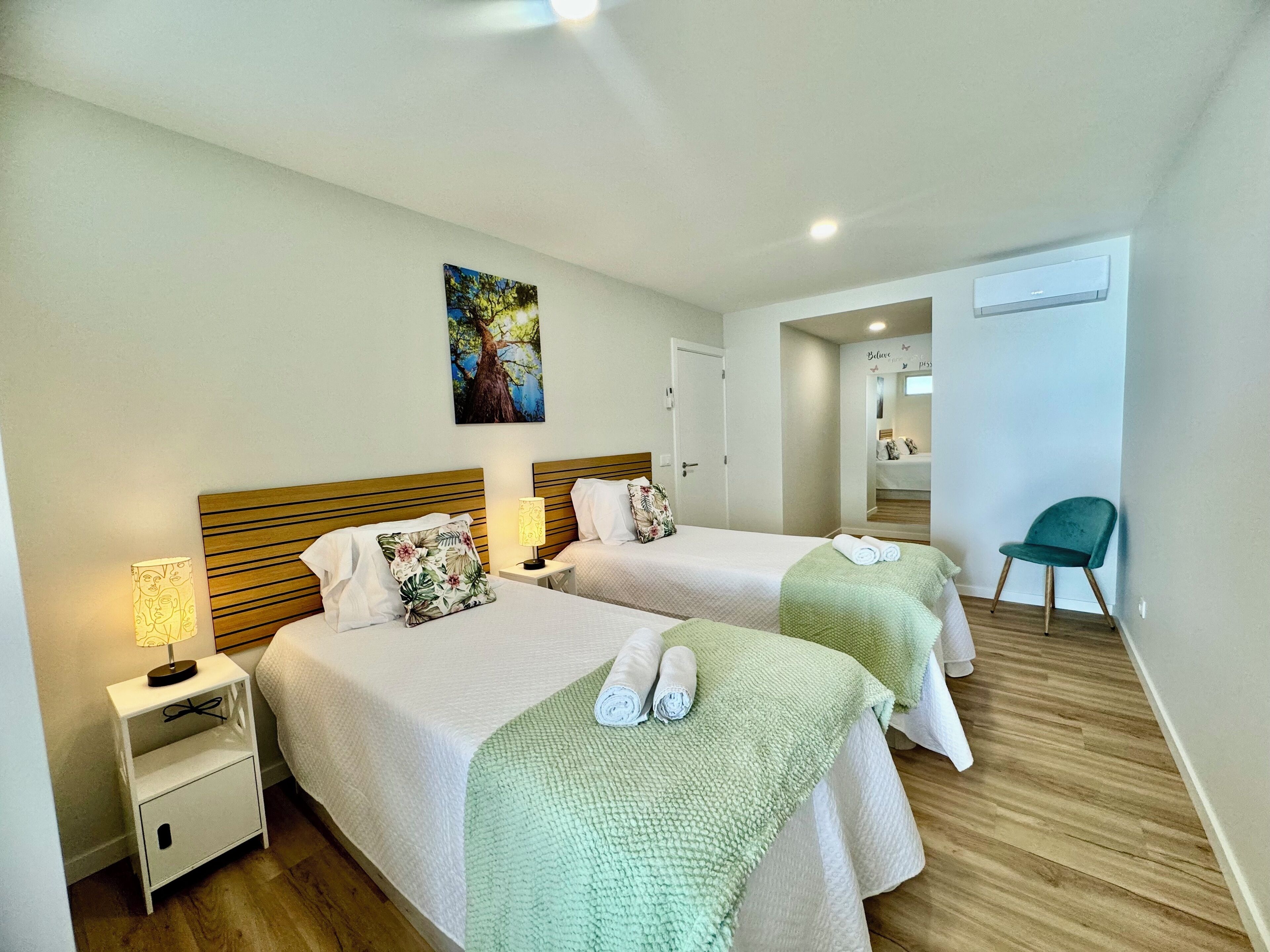 A hotel room with two beds, a nightstand with a lamp, a chair, and a painting on the wall.