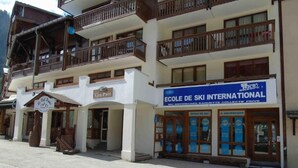 A multi-story building with a ski school sign, wooden balconies, and a ski lift visible in the background.