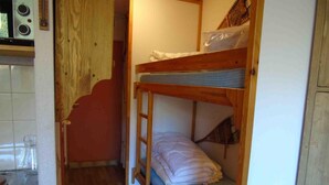 A compact room with a bunk bed, a small kitchenette, and a wooden staircase.