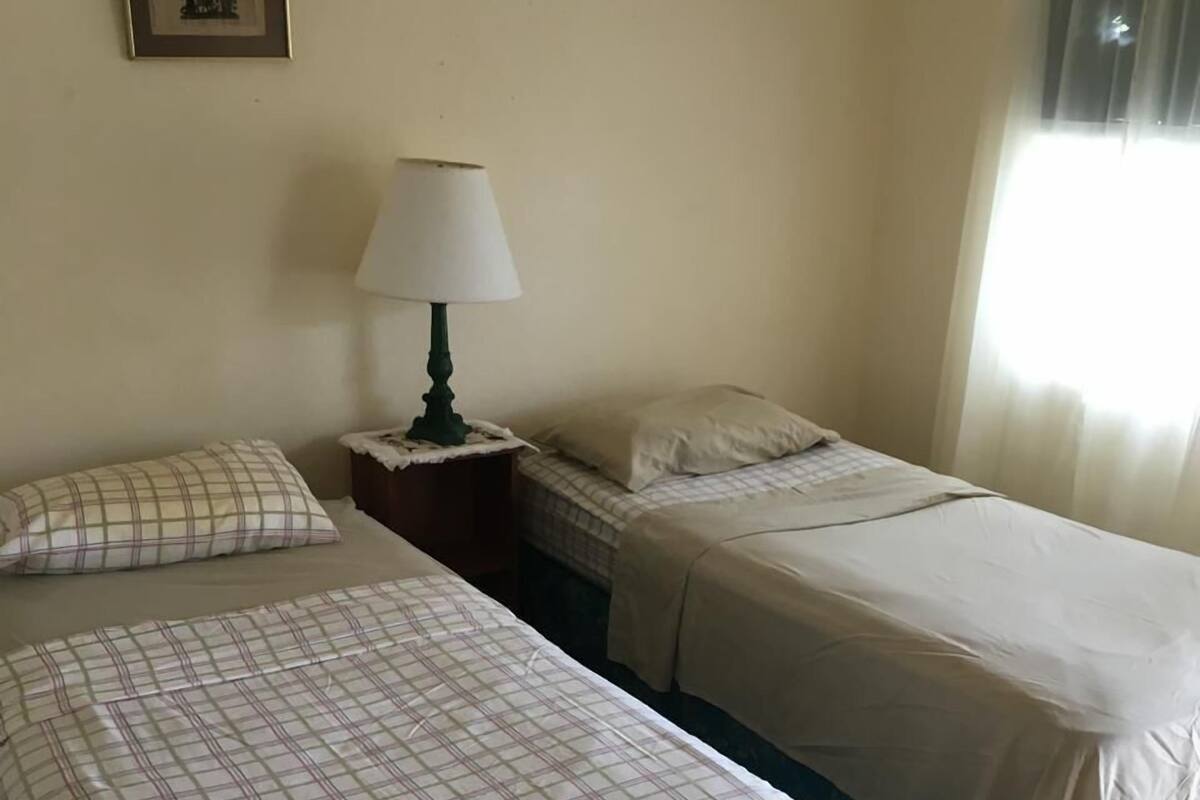 A hotel room with two beds, a nightstand with a lamp, a framed picture on the wall, and a window with curtains.