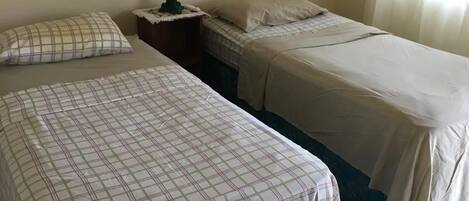 Une chambre d’hôtel avec deux lits, une table de chevet avec une lampe, un tableau encadré au mur et une fenêtre avec des rideaux.