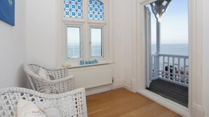 Quarto com vista para o mar, mobiliário de vime e janela com a inscrição 'Beach'.