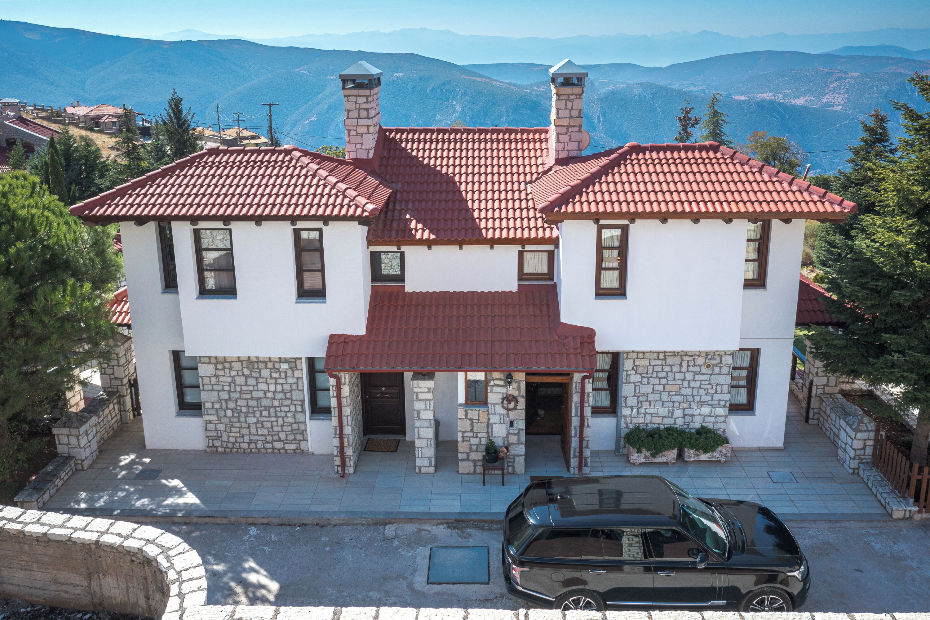 A two-story house with a red-tiled roof, stone facade, and a car parked in front.