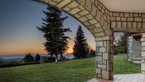 A stone archway leading to a grassy area with a sunset view. - Sky Shades Villa in Arachova (Arachova)