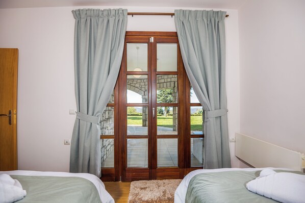 Un dormitorio con dos camas, una puerta de madera y un amplio ventanal que da a un espacio al aire libre.