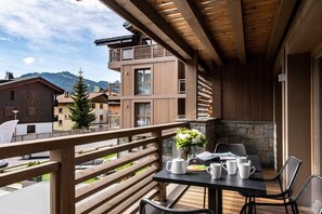 A balcony with a table set for two, a vase of flowers, and a stone wall. - Wifi, 200m from ski slopes, 1st floor, sauna, hammam, balcony, fireplace or stove, parking, tv (Les Gets)