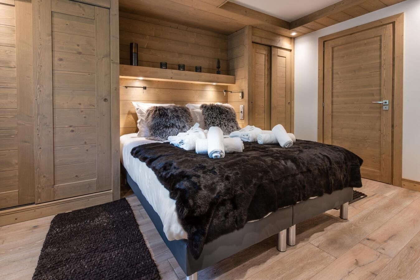A bedroom with a large bed, wooden walls, and a dark rug.