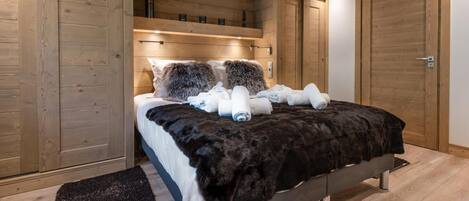 A bedroom with a large bed, wooden walls, and a dark rug.