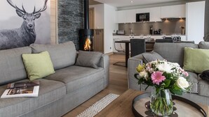Una sala de estar moderna con chimenea, sofás grises y un comedor con una cocina al fondo.