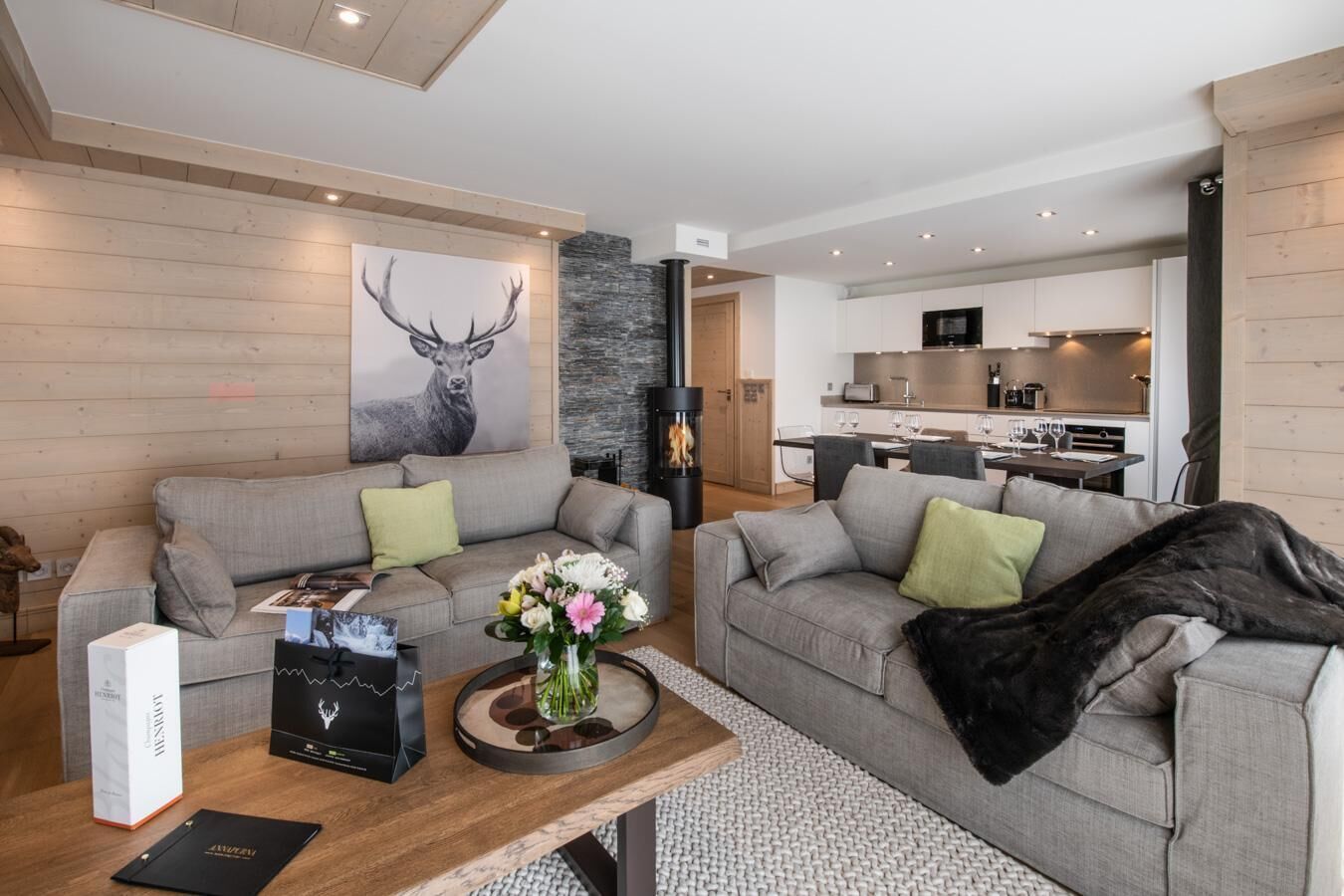 A modern living room with two grey sofas, a coffee table with a vase of flowers, and a fireplace.