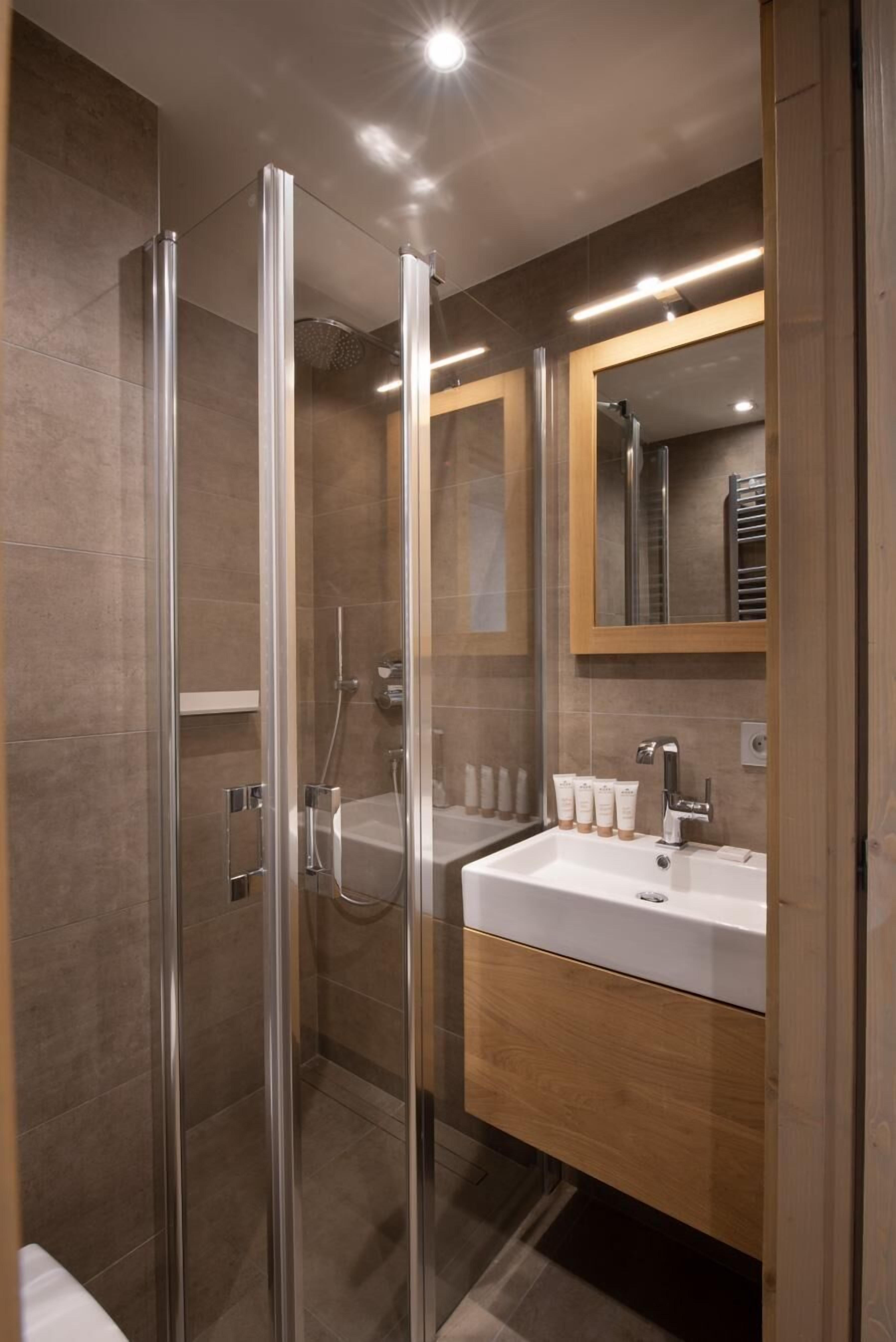 A modern bathroom with a glass-enclosed shower, a white sink, and a wooden vanity.