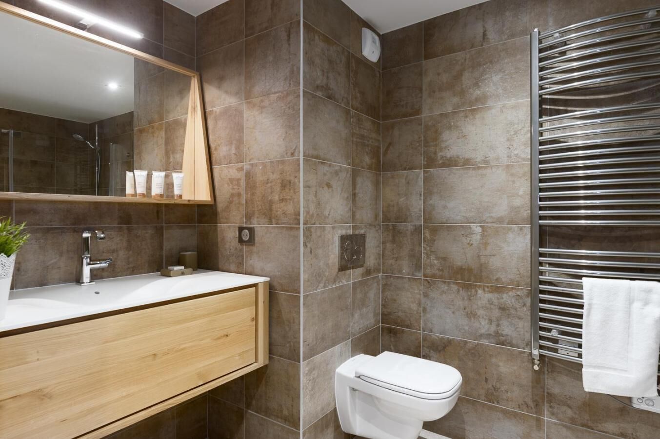 A modern bathroom with a wooden vanity, a white sink, a toilet, and a towel rack.