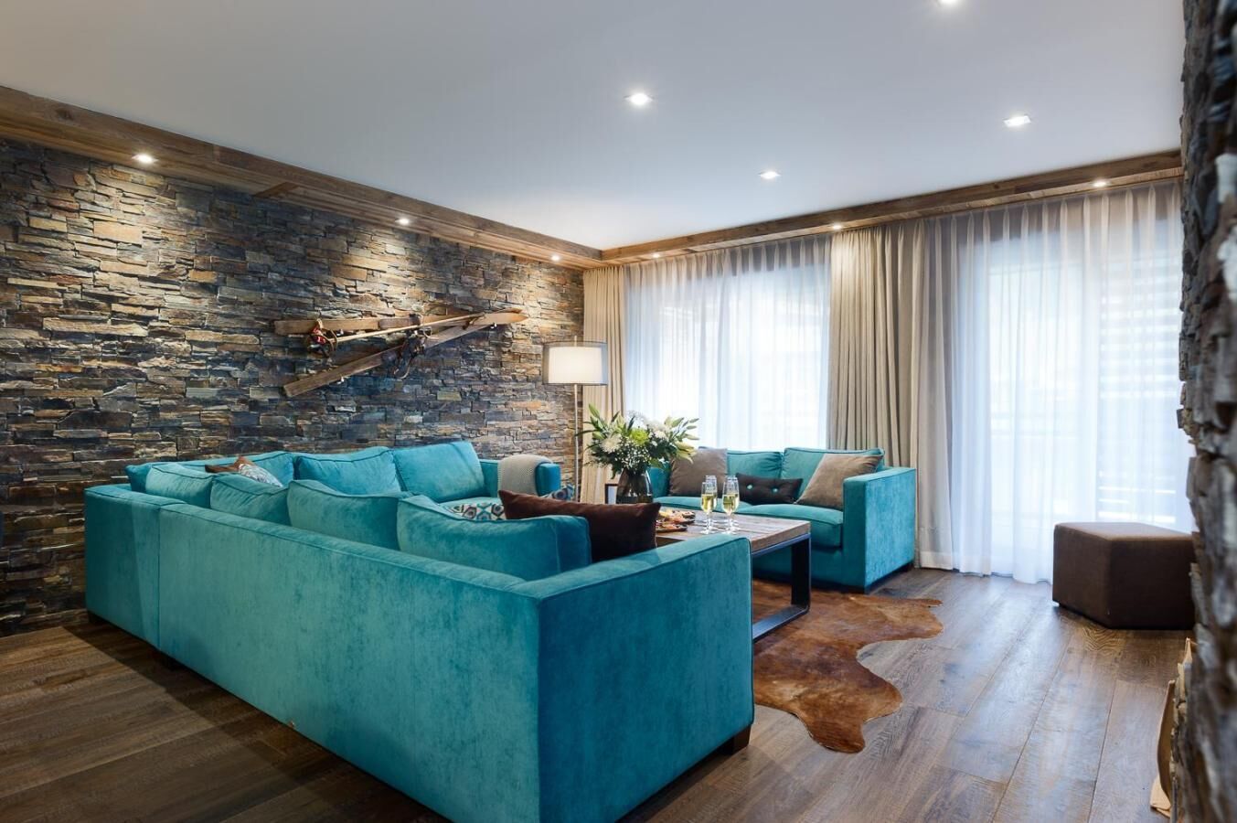 A modern living room with a stone wall, a blue sofa set, a wooden coffee table, and a leather rug.