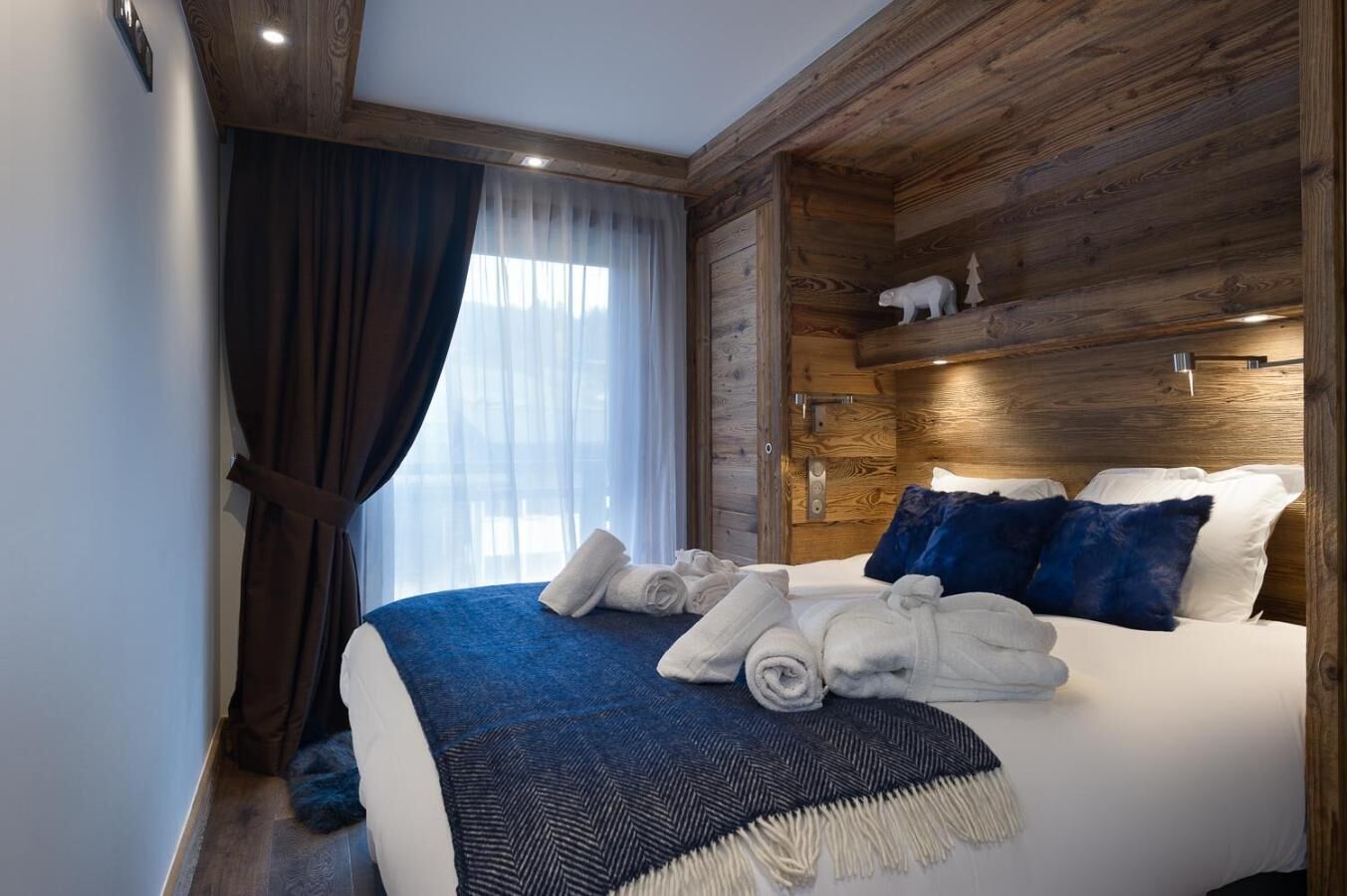 Une chambre d’hôtel avec une tête de lit en bois, un grand lit avec une literie blanche et bleue, un plaid bleu et une paire de serviettes enroulées posées sur le lit.