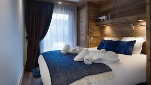 Habitación de hotel con cabecera de madera, una cama grande con ropa de cama blanca y azul, una manta azul y un par de toallas enrolladas sobre la cama.