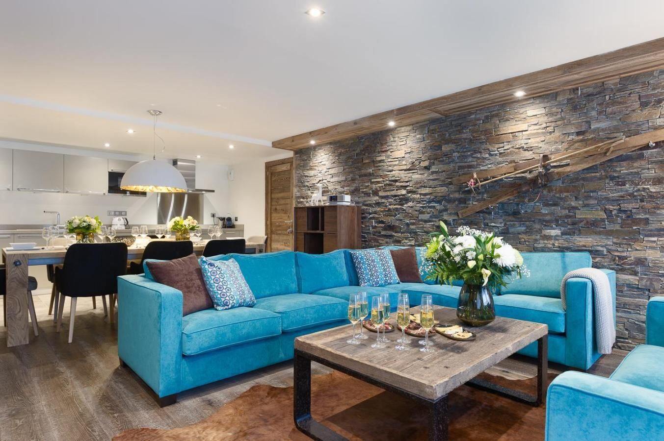 A modern living room with a blue sofa, a wooden coffee table, and a stone wall.