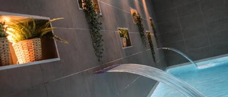 A modern bathroom with a large bathtub, grey tiled walls, and potted plants in built-in niches.