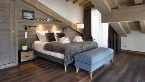 A bedroom with a large bed, wooden beams, a small bedside table with a lamp, and a window with curtains. - Wifi, 200m from ski slopes, 3rd floor, sauna, hammam, balcony, fireplace or stove, parking, tv (Les Gets)