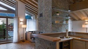 A modern kitchen with a stone wall, wooden beams, and a glass shelf. - Wifi, resort center, 3rd floor, view mountain, sauna, hammam, terrace, balcony, fireplace or stove (Les Gets)