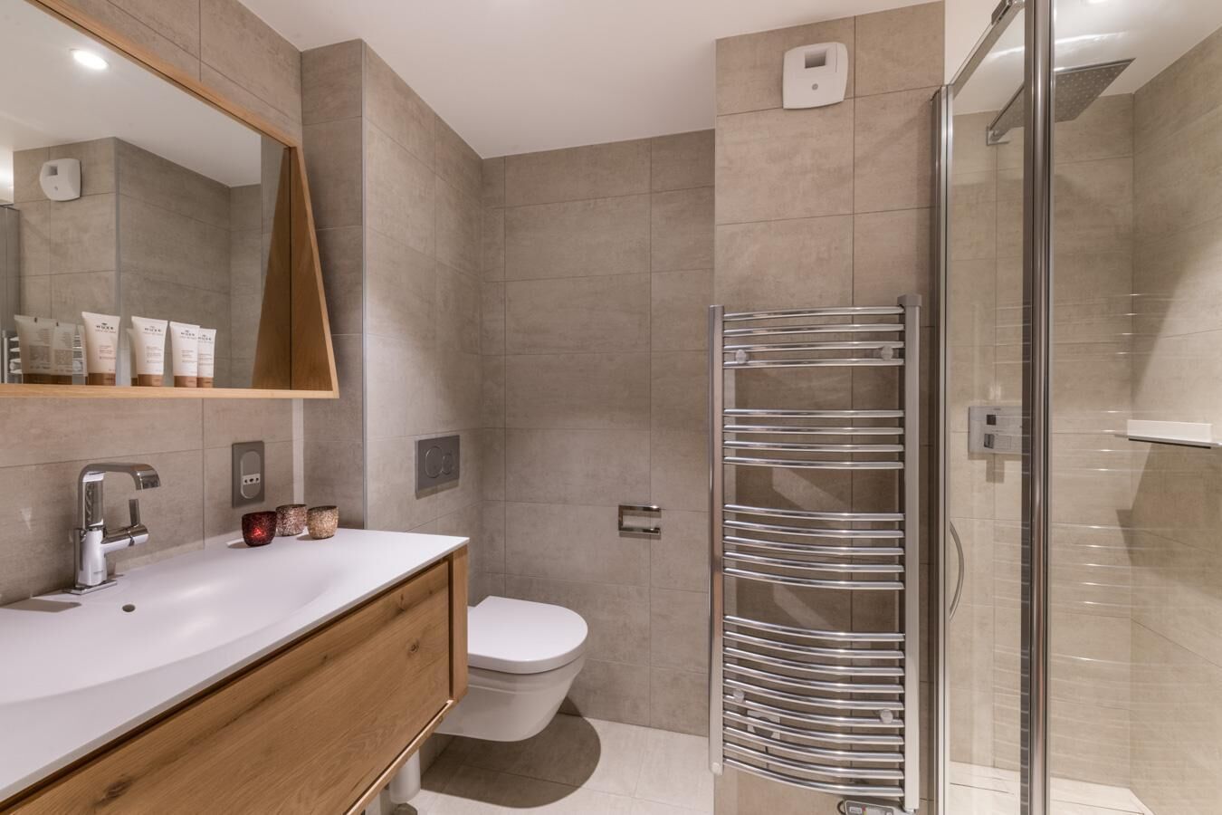 A modern bathroom with a large mirror, a sink, a toilet, and a glass-enclosed shower area.