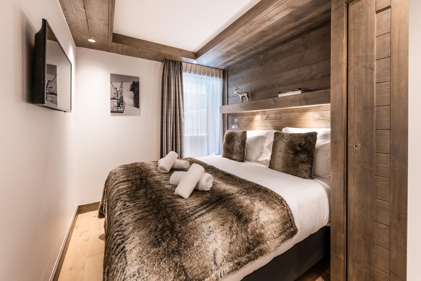 Una habitación de hotel moderna con cabecera de madera, una cama grande con manta mullida y un televisor de pantalla plana montado en la pared.