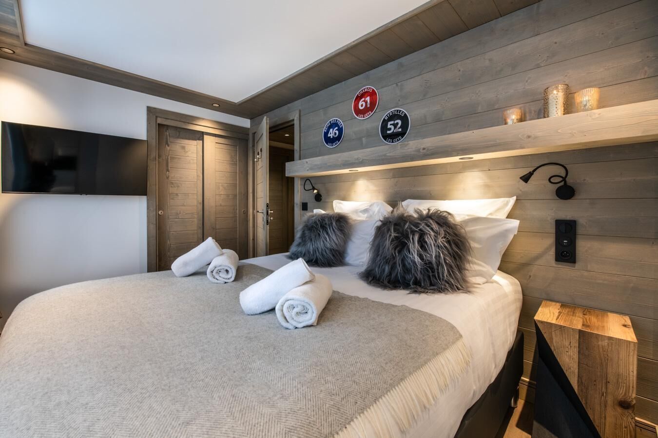 Una habitación de hotel moderna con una cama grande, cabecero de madera y un televisor montado en la pared.