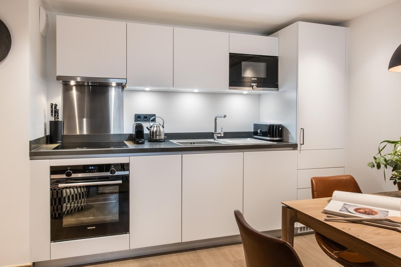 Cozinha moderna com eletrodomésticos de aço inoxidável, forno embutido e área de jantar com mesa e cadeiras.