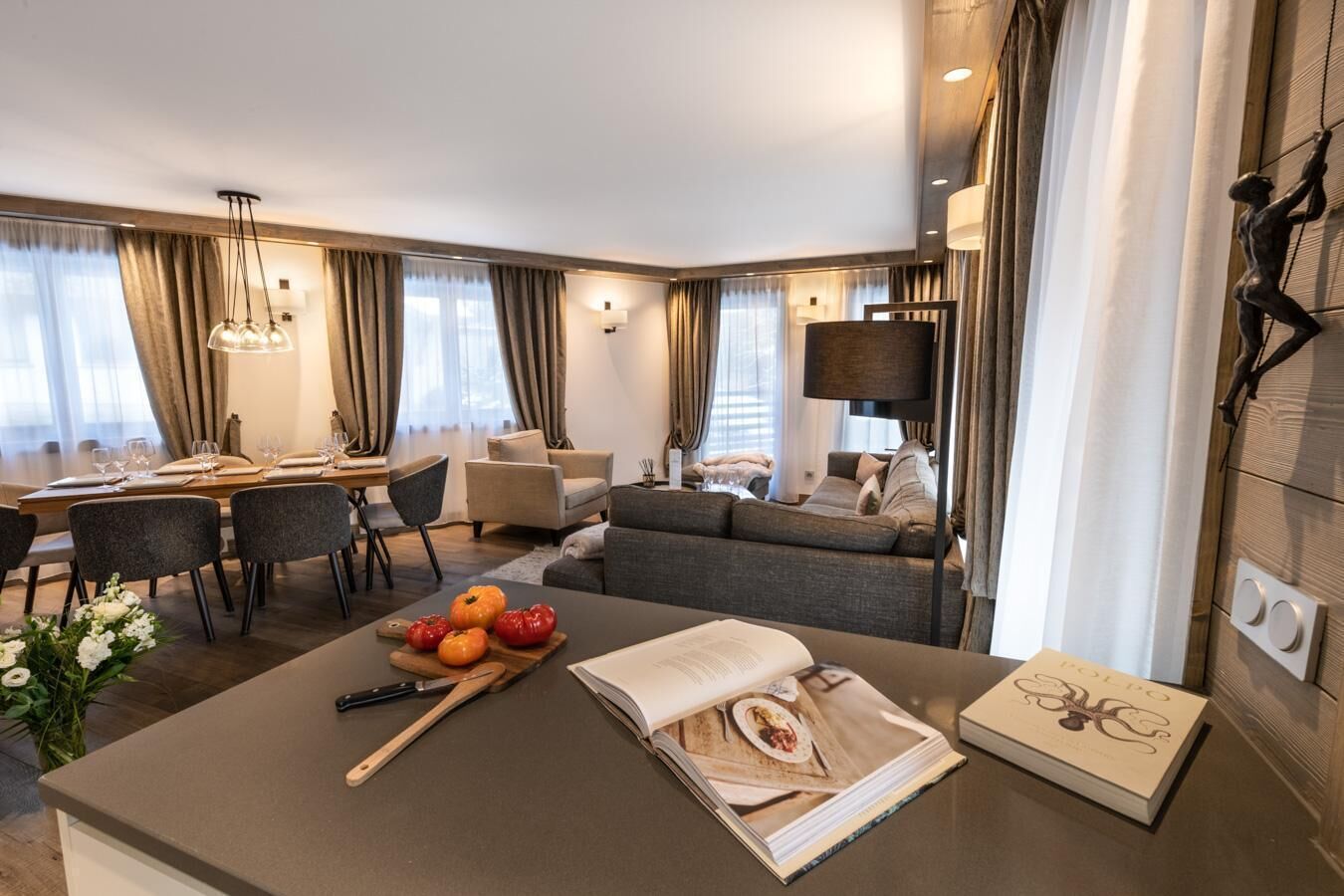 A modern hotel room with a dining area, a sofa, and a large window with curtains.