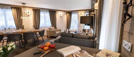 A modern hotel room with a dining area, a sofa, and a large window with curtains.