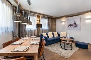 Una sala de estar moderna con comedor, que presenta una mesa de madera preparada para cuatro, un sofá azul con cojines mullidos y una mesa de centro redonda.