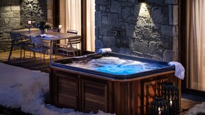 A hot tub with a wooden exterior, surrounded by snow, with a stone wall and a table with chairs in the background. - Wifi, 200m from ski slopes, Ground floor, terrace, parking, tv, 81m², Les Gets (Les Gets)