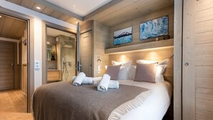 A modern hotel room with a large bed, wooden paneling, a glass shower enclosure, and artwork on the wall. - Wifi, 200m from ski slopes, Ground floor, terrace, parking, tv, 81m², Les Gets (Les Gets)