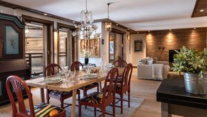 Un coin repas avec une table en bois, des chaises et un lustre. Le salon comprend un canapé et une plante.
