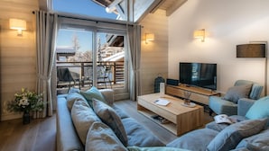 En moderne stue med en stor sofa, et sofabord og et fjernsyn. Der er en balkon med udsigt over snedækkede bygninger.