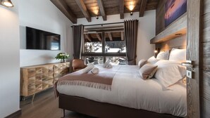 Quarto de hotel moderno com uma cama grande, cabeceira de madeira e vista para uma paisagem nevada pela janela.