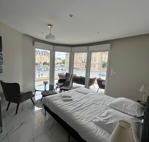 Une chambre d’hôtel avec un lit, une chaise, une petite table et une vue sur la ville grâce à de grandes fenêtres.
