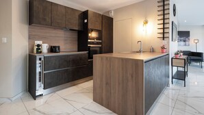 Cocina moderna con armarios oscuros, una isla central y una zona de comedor con sofá y mesa.
