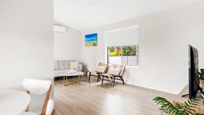A modern living room with a sofa, two armchairs, a coffee table, and a TV on a wooden stand. - This is Livin' - Fire Pit - 3 Mins Walk to Beach (Culburra Beach)