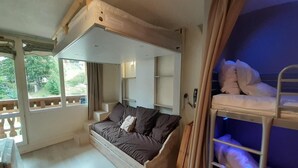 Una habitació amb un llit doble de fusta, un sofà-llit i una finestra amb vista a vegetació.