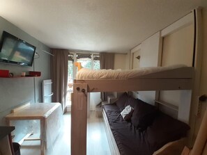 Una camera compatta con letti a castello, una scrivania piccola e una TV fissata alla parete.