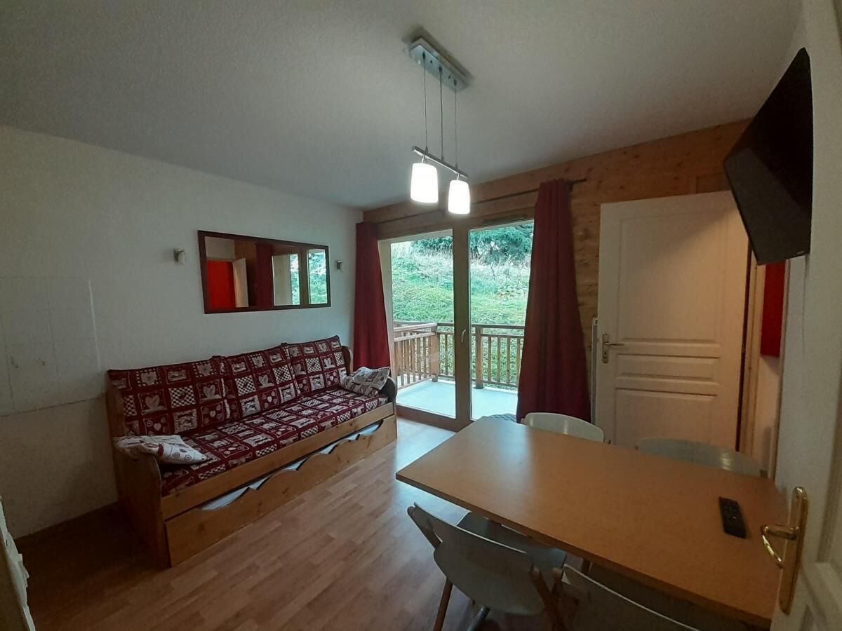 A room with a wooden sofa, a dining table, and a sliding glass door leading to an outdoor area.