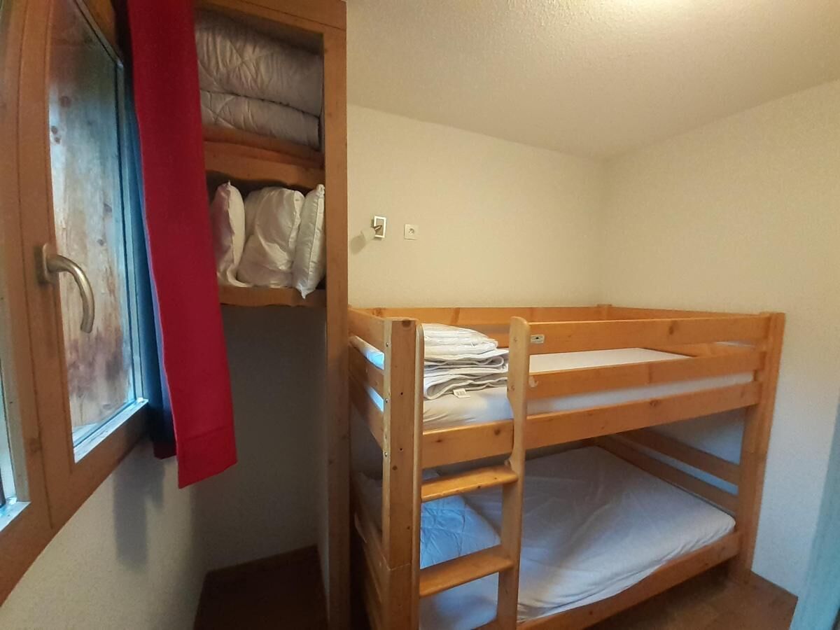 A bunk bed in a small room with a window and a red curtain.