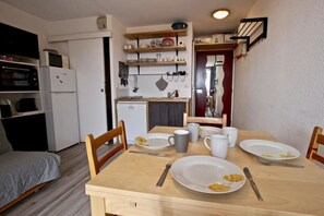 A compact kitchen with a dining table set for two, a refrigerator, and a microwave.
