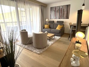 A modern living room with a grey sofa, two round ottomans, a wooden coffee table, and a white shag rug.