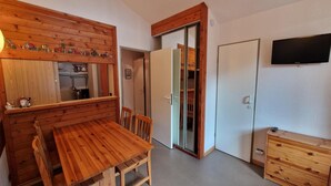 Una mesa de comedor de madera con sillas, un mueble de madera, un televisor y una puerta corrediza que da a la cocina.