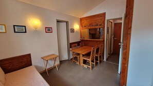 Una habitación compacta con cama, una mesita pequeña, una mesa de comedor con sillas y un rincón de cocina.