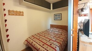 A bedroom with a bed, a wall-mounted shelf, a picture, and a door leading to another room. - 4th floor, view valley, balcony, tv, ski locker, 23m², Valfréjus (Valfréjus)