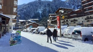 A snow-covered street with buildings and parked cars, a clear sky, and a mountainous backdrop. - 4th floor, view valley, balcony, tv, ski locker, 23m², Valfréjus (Valfréjus)