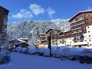 A snow-covered resort with wooden buildings, a ski lift, and a mountain backdrop.